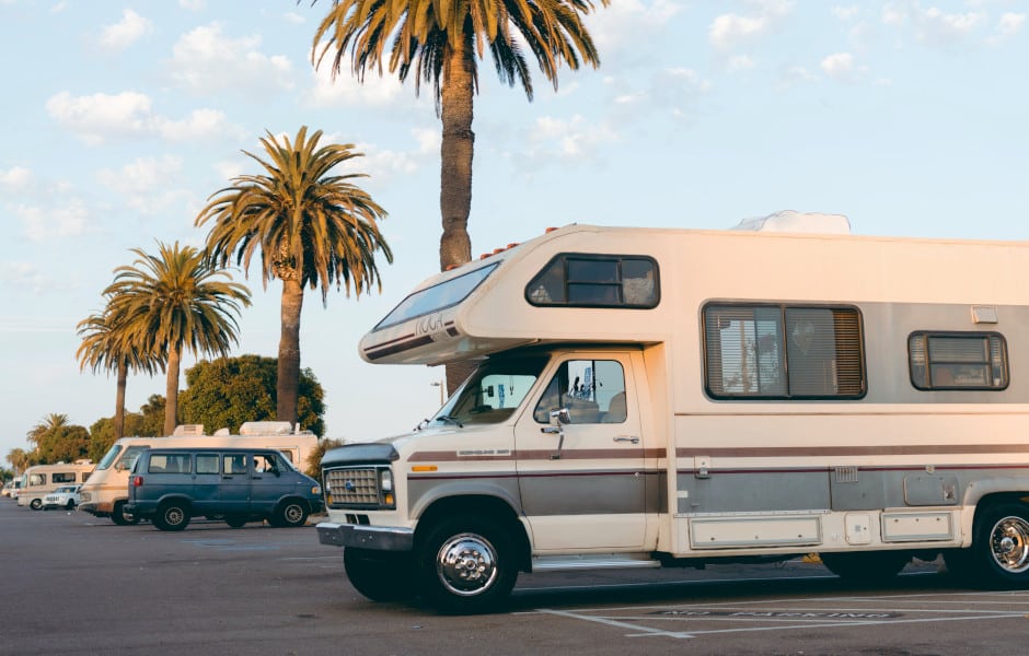 Motorhomes and a campervan parked side by side in a seaside car park at sunset