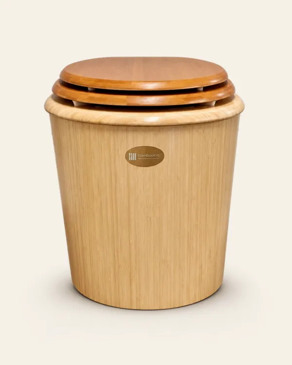 A Bambooloo seen from the front on a plain cream background: a tapered bamboo body with an oval bambooloo badge, a rounded rim, and the seat and lid closed over small white stops